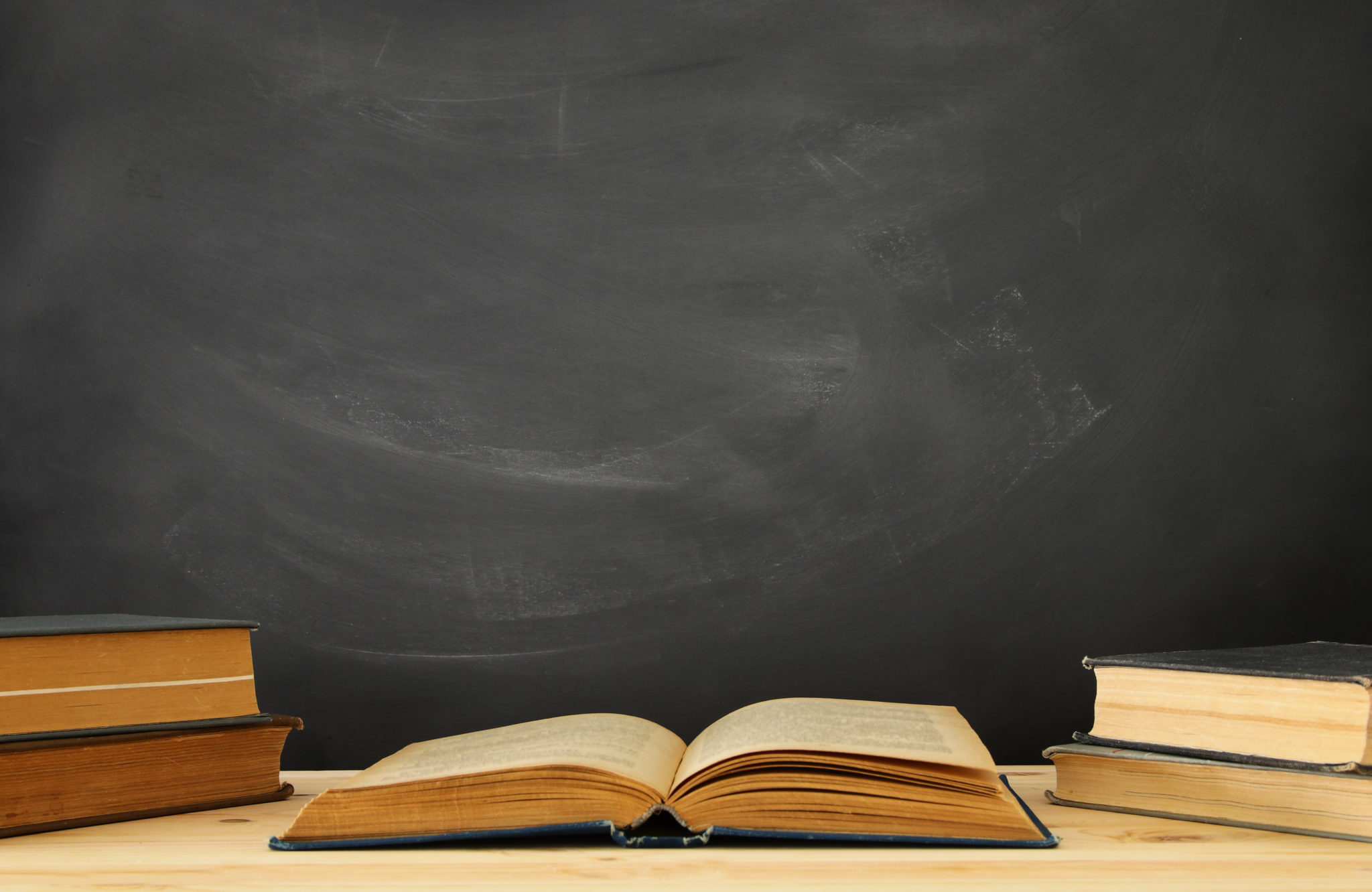 stack of books over wooden desk in front of blackboard