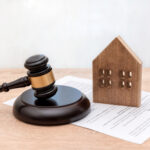 Wooden House Model with Judge's Gavel and Legal Document on Table